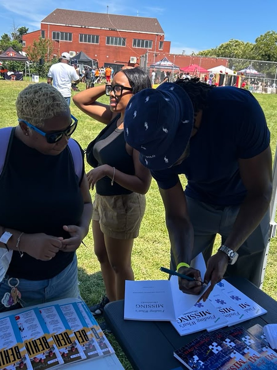 Marco Lomax signing Finding What's Missing books for community members at an outdoor event